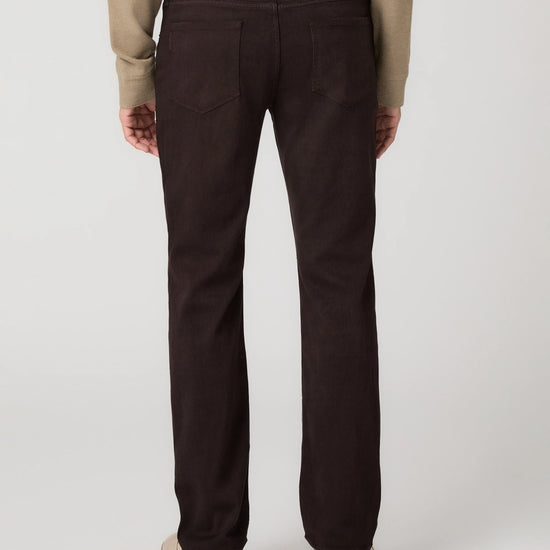 Rear view of a person wearing dark brown straight-leg jeans with a beige long-sleeve top and beige platform shoes, against a light gray studio background.