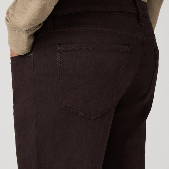 Close-up back view of a person wearing dark brown or very deep espresso corduroy trousers, paired with a beige sweater, against a light gray studio background.