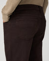 Close-up back view of a person wearing dark brown or very deep espresso corduroy trousers, paired with a beige sweater, against a light gray studio background.