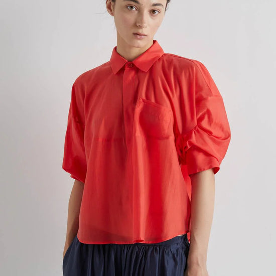 Person wearing a red blouse with puffed sleeves on a plain background