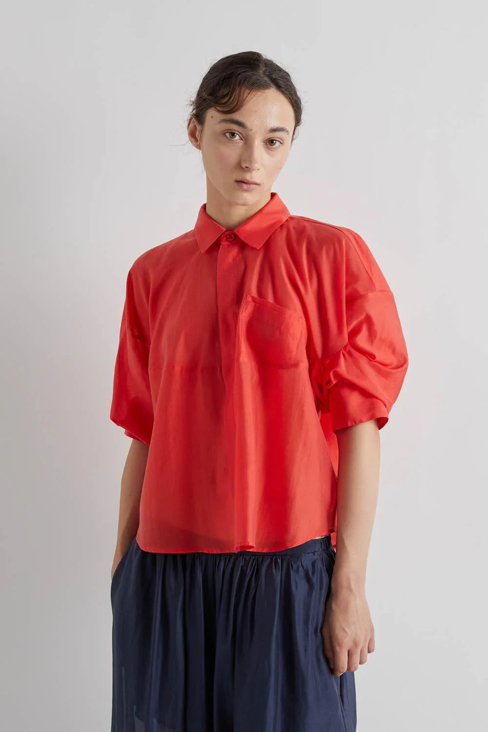 Person wearing a red blouse with puffed sleeves on a plain background