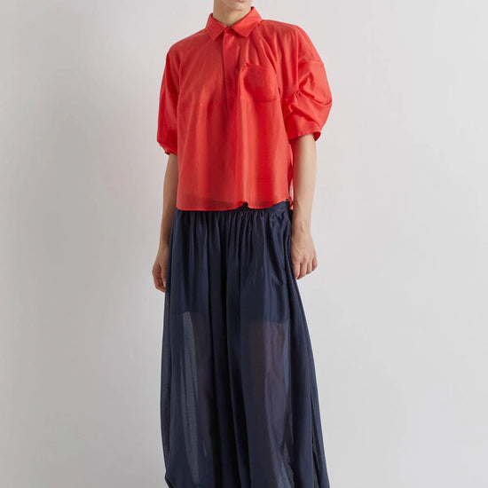 Person wearing a red blouse and navy pants on a light gray background