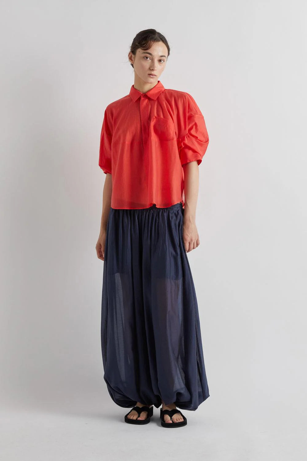 Person wearing a red blouse and navy pants on a light gray background