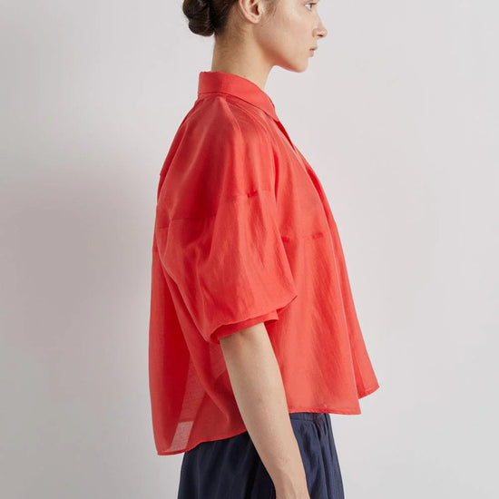 Person wearing a red shirt and dark pants against a plain background