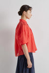 Person wearing a red shirt and dark pants against a plain background