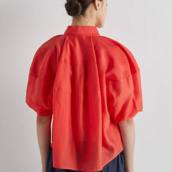 Person wearing a red blouse with puff sleeves on a plain background
