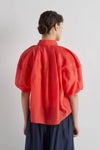 Person wearing a red blouse with puff sleeves on a plain background