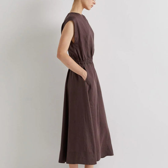 Woman wearing a brown linen dress against a plain background