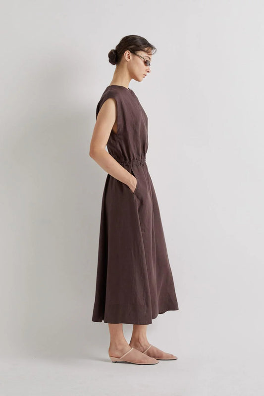 Woman wearing a brown linen dress against a plain background