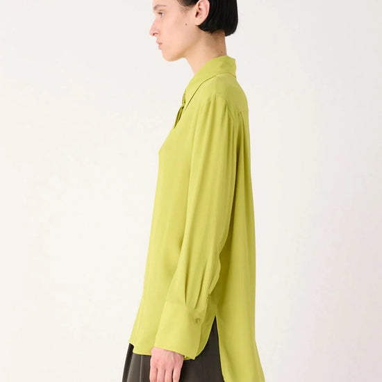 A model shown in profile wearing a lime green long-sleeve button-up shirt and dark olive pants, photographed against a clean white studio background.