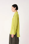 A model shown in profile wearing a lime green long-sleeve button-up shirt and dark olive pants, photographed against a clean white studio background.