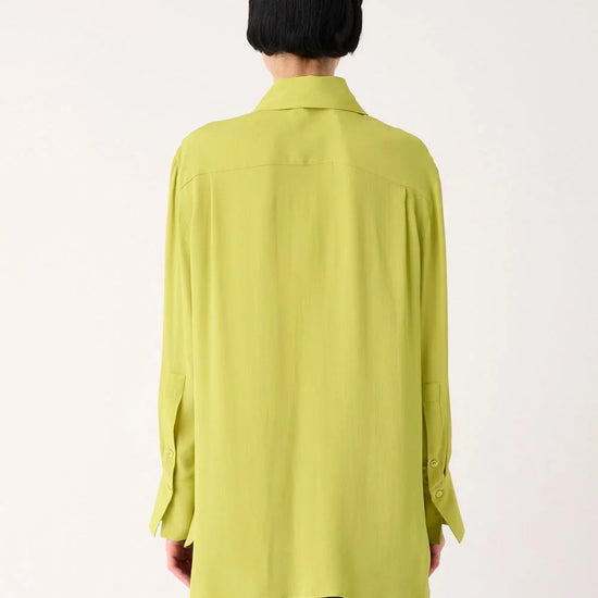 A person shown from the back wearing a light yellow-green long-sleeve button-up shirt and dark gray cargo pants against a plain white studio background.