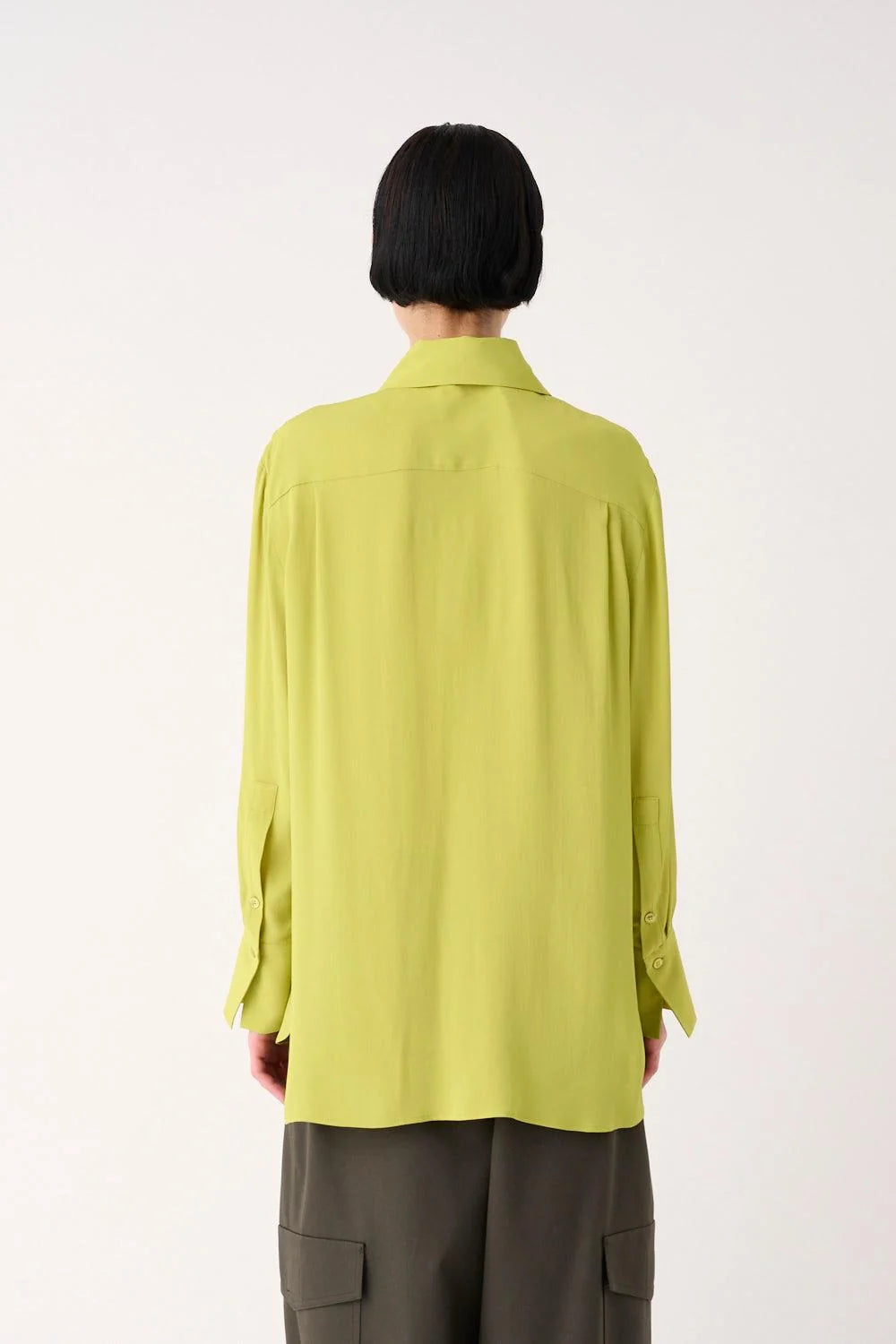 A person shown from the back wearing a light yellow-green long-sleeve button-up shirt and dark gray cargo pants against a plain white studio background.
