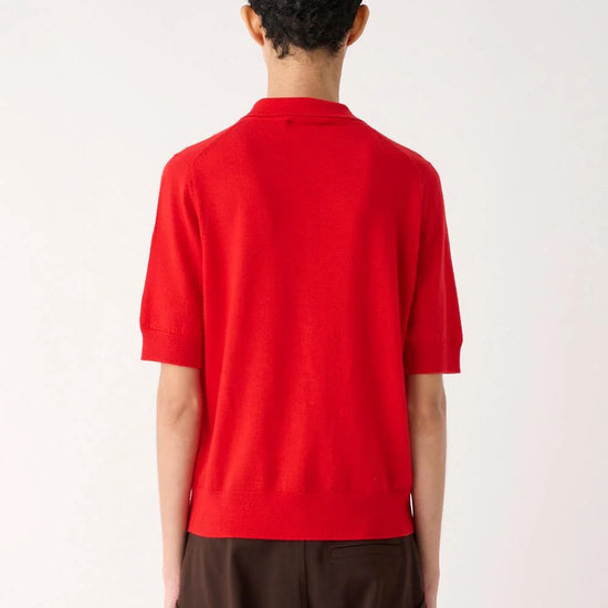 A model shown from the back wearing a bright red short-sleeve knit top and dark brown wide-leg trousers, set against a plain off-white studio background.