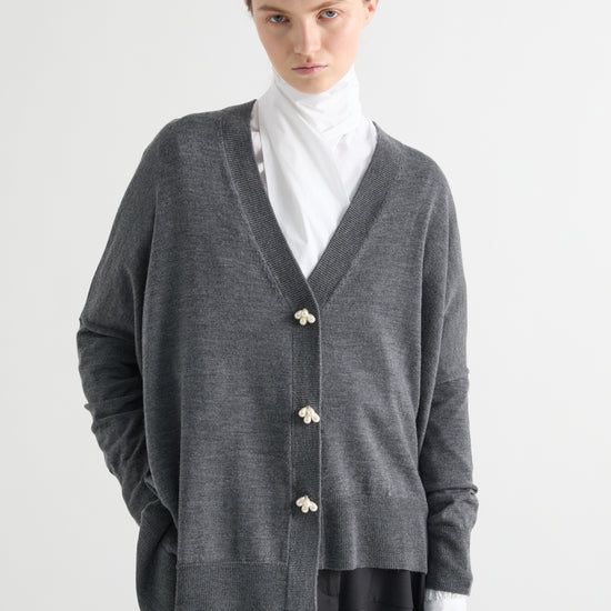 Person wearing a gray cardigan with white buttons on a white background