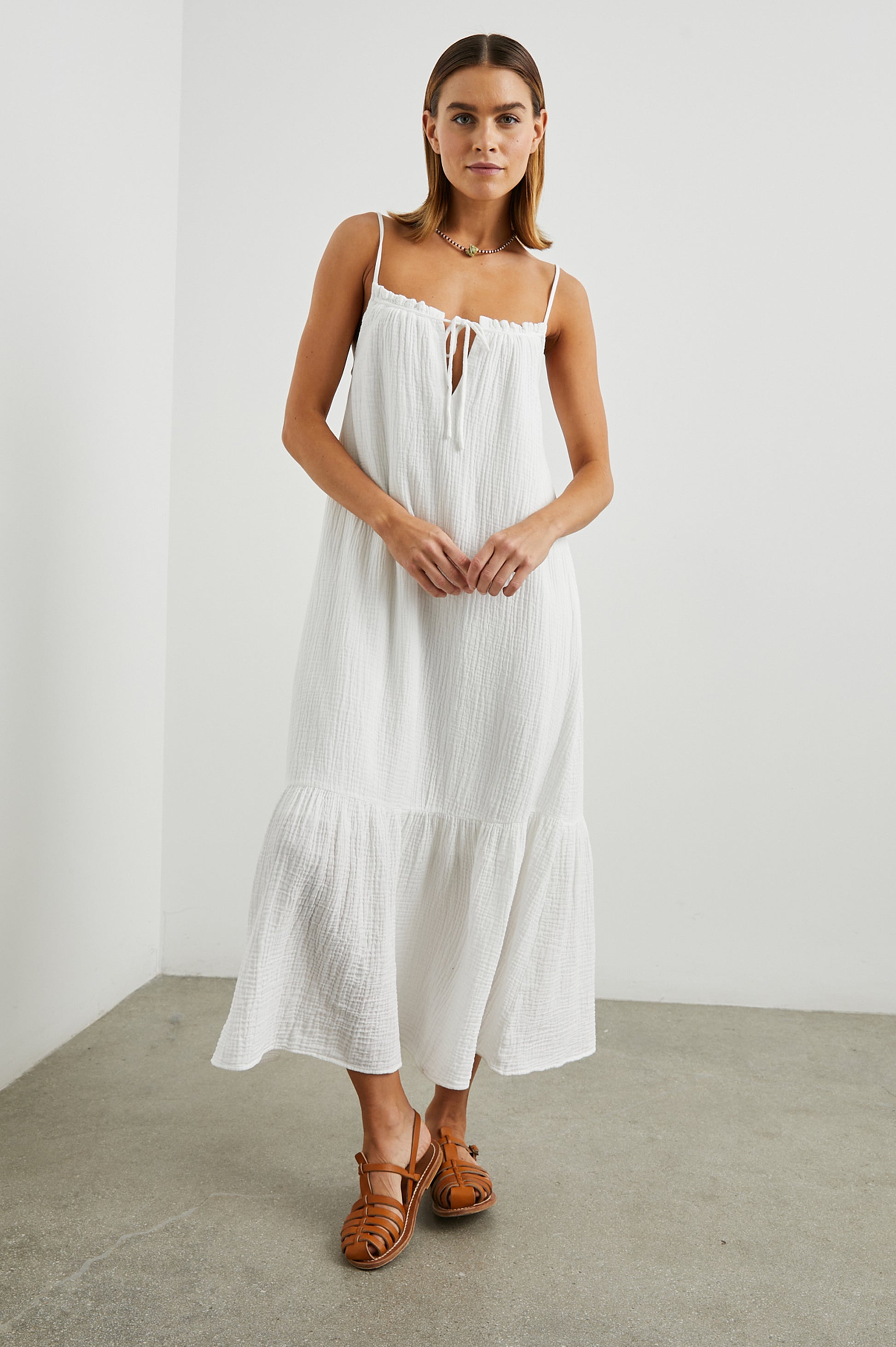 Strappy white cotton muslin dress with tie detail at the neckline and a deep ruffle at the hem