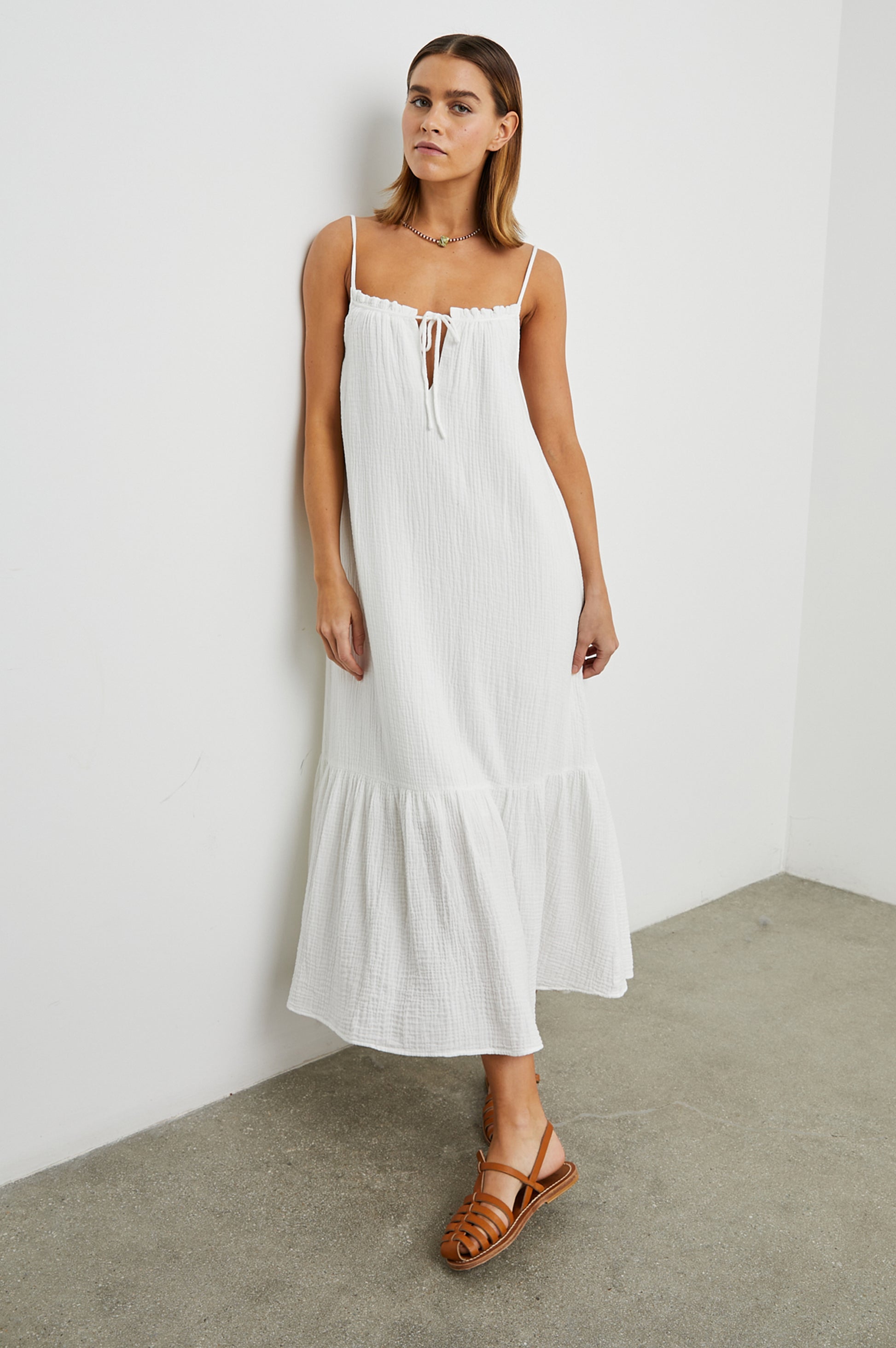 Strappy white cotton muslin dress with tie detail at the neckline and a deep ruffle at the hem