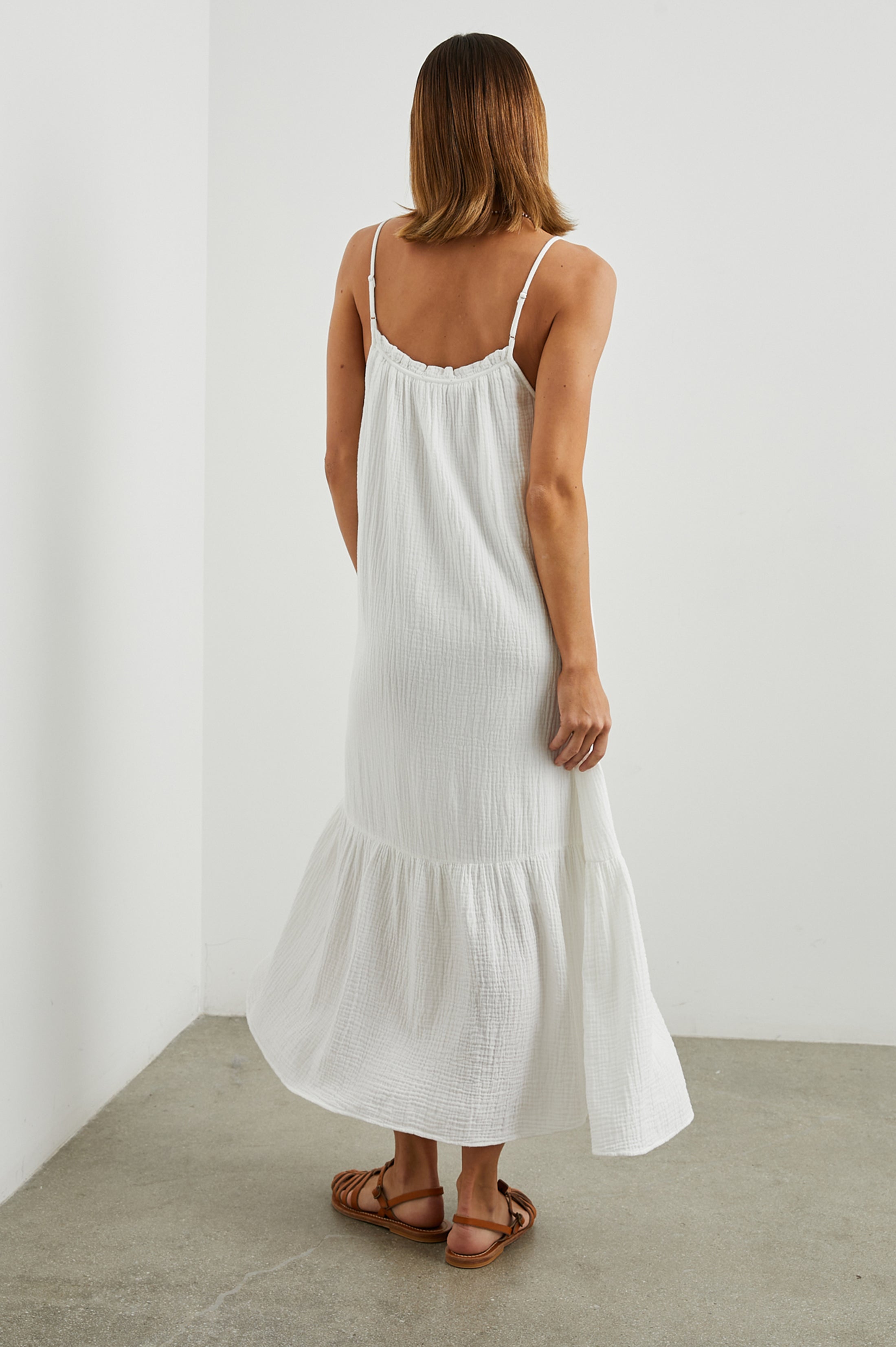 Strappy white cotton muslin dress with tie detail at the neckline and a deep ruffle at the hem rear view