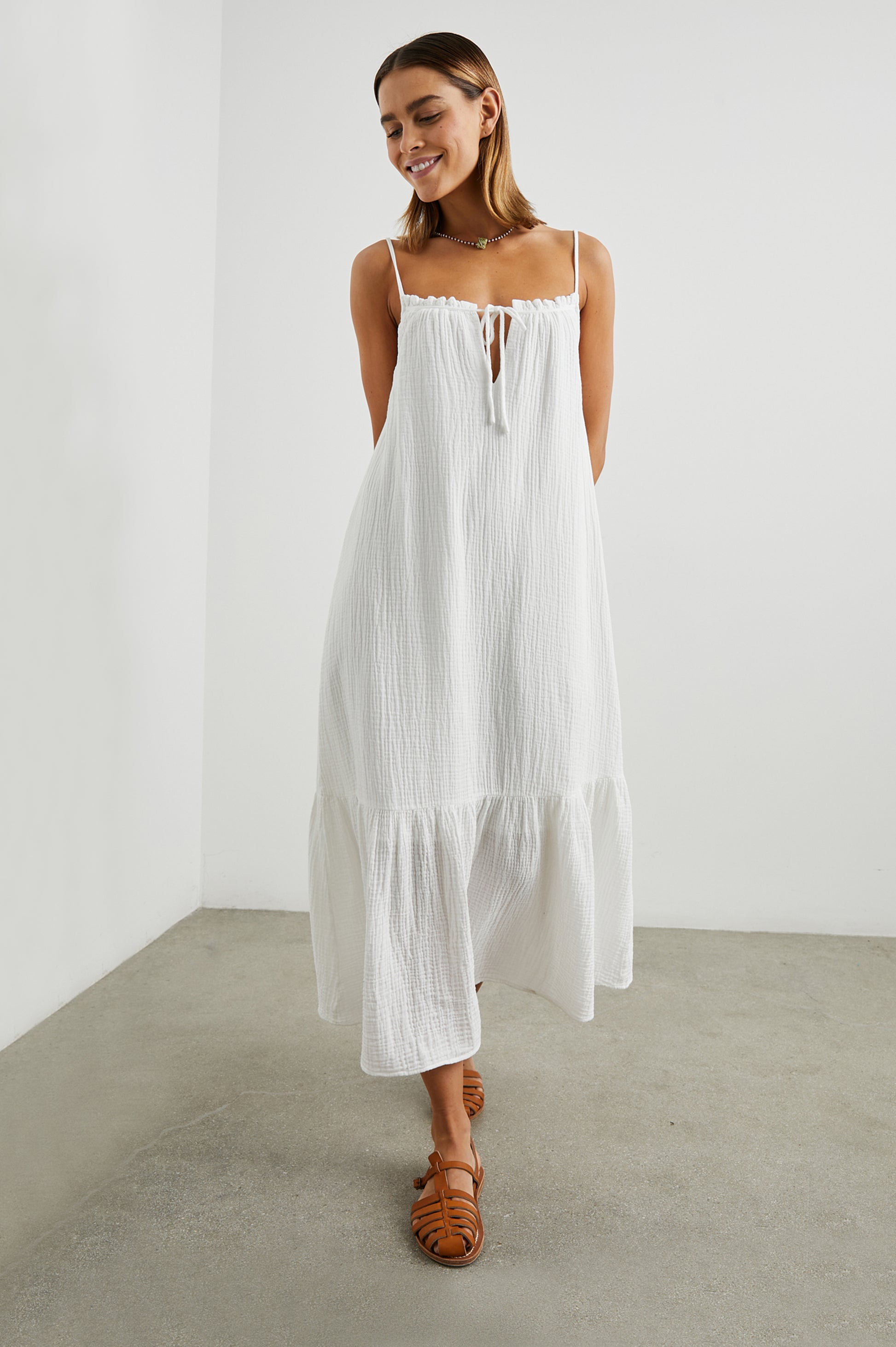 Strappy white cotton muslin dress with tie detail at the neckline and a deep ruffle at the hem