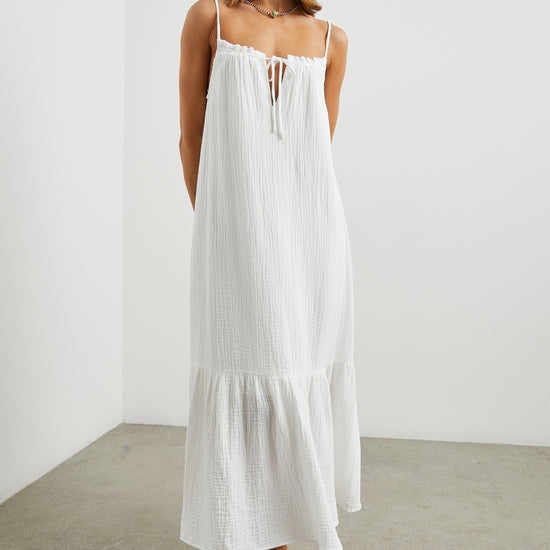 Strappy white cotton muslin dress with tie detail at the neckline and a deep ruffle at the hem