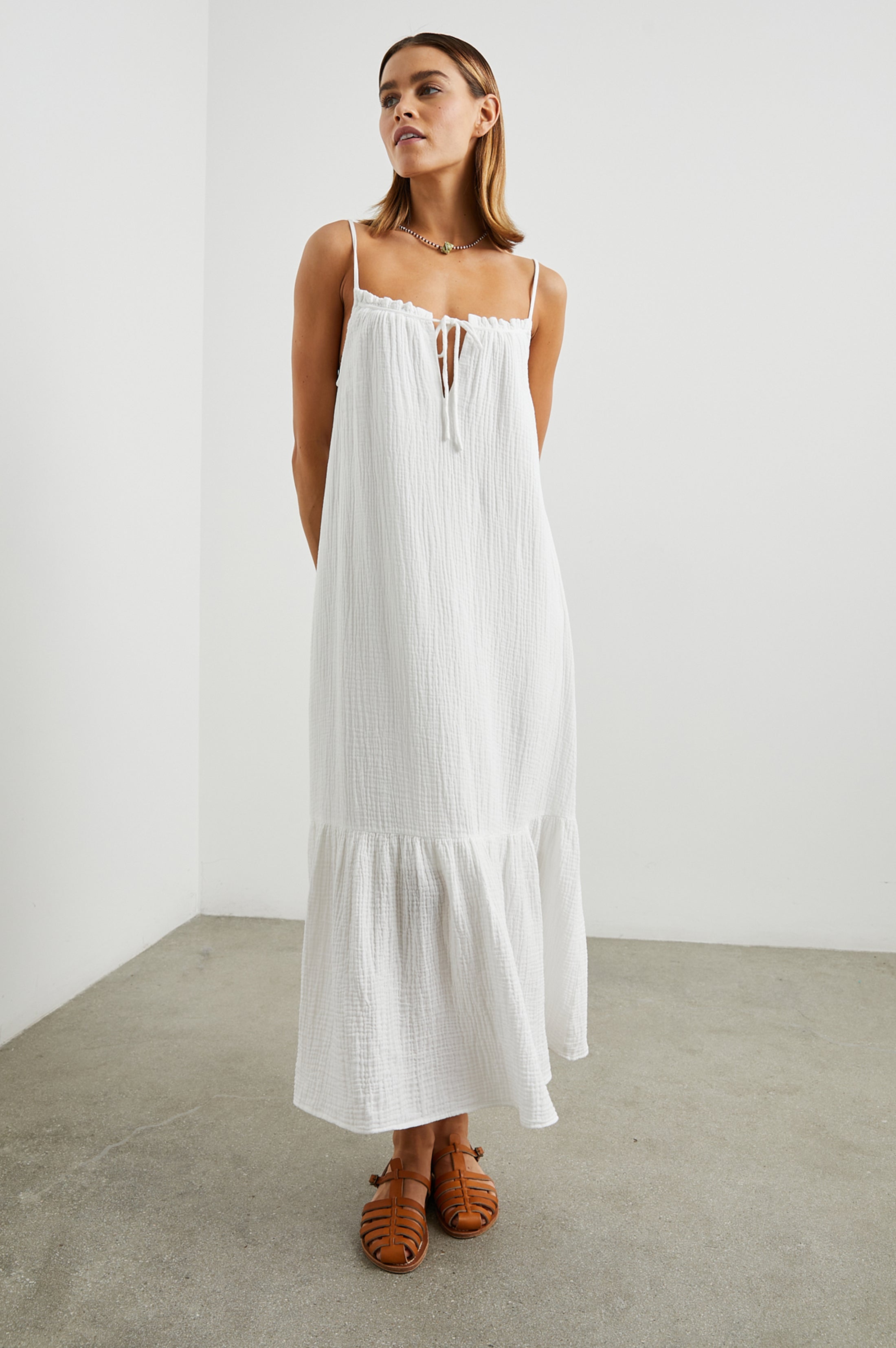 Strappy white cotton muslin dress with tie detail at the neckline and a deep ruffle at the hem