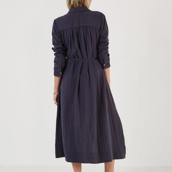 Woman wearing a long dark blue dress by Mondo Corsini on a white background. Rear View.