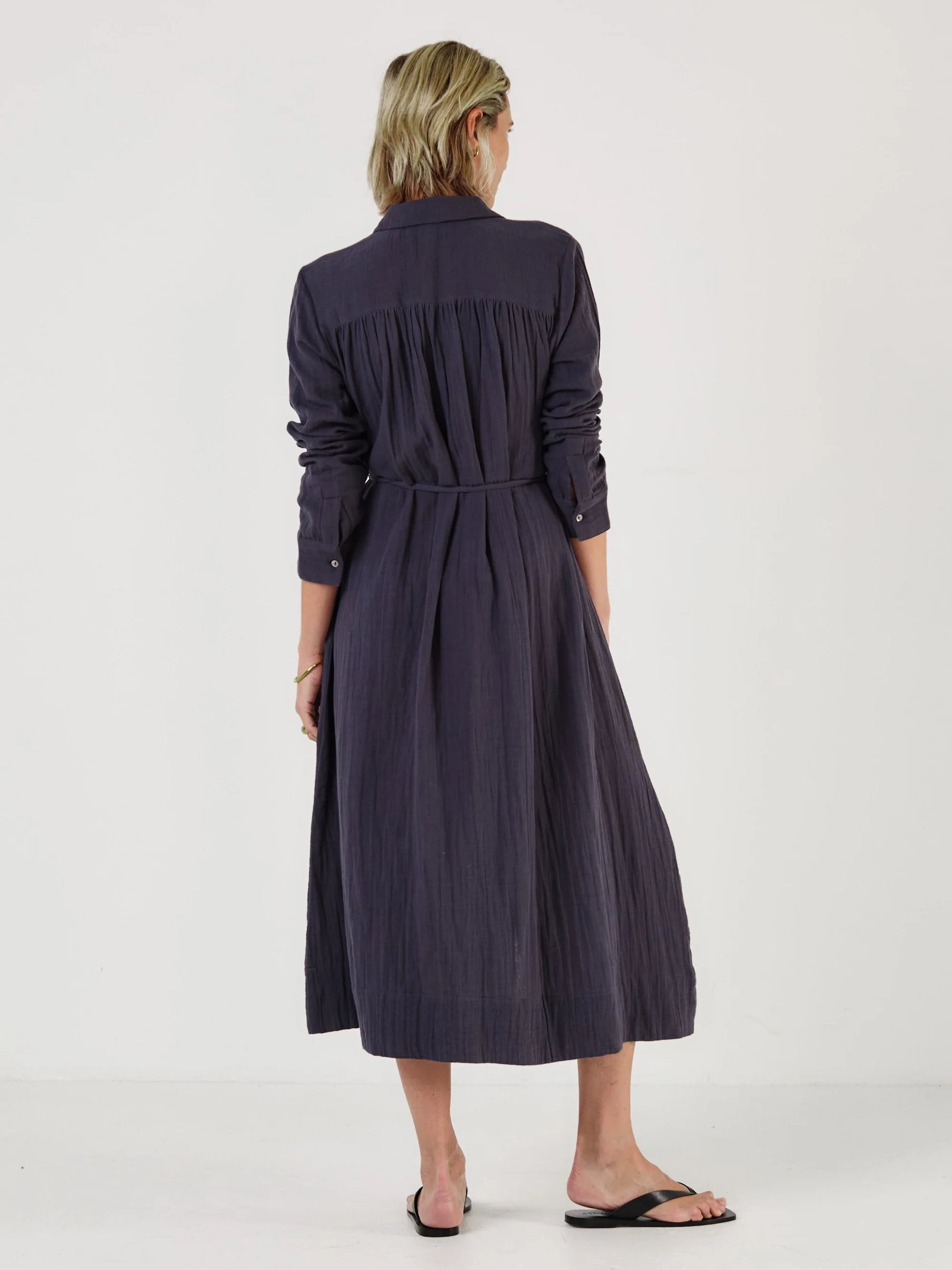 Woman wearing a long dark blue dress by Mondo Corsini on a white background. Rear View.
