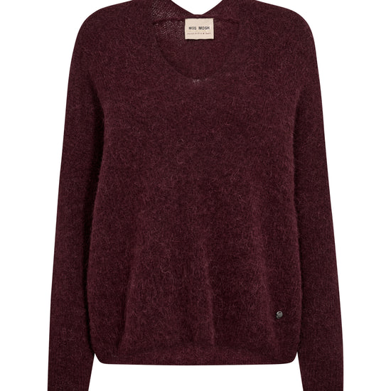 A dark burgundy knit sweater with a crew neck and long sleeves, shown flat against a plain white background. A small beige brand label is visible at the inner collar, and a tiny dark button detail is near the lower right hem.