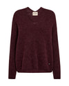 A dark burgundy knit sweater with a crew neck and long sleeves, shown flat against a plain white background. A small beige brand label is visible at the inner collar, and a tiny dark button detail is near the lower right hem.
