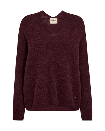 A dark burgundy knit sweater with a crew neck and long sleeves, shown flat against a plain white background. A small beige brand label is visible at the inner collar, and a tiny dark button detail is near the lower right hem.