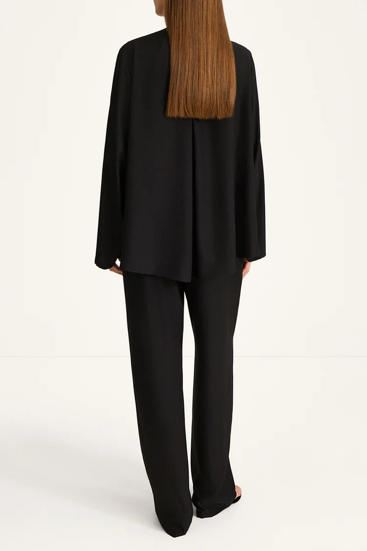 A model shown from the back wearing a black draped long-sleeve blazer and matching wide-leg trousers against a clean white studio background.