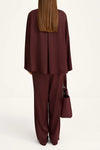 Person wearing a burgundy outfit with a matching handbag on a white background
