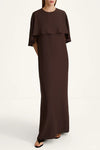 A woman modeling a floor-length dark brown dress with a layered ruffle neckline and short flutter sleeves, photographed against a plain off-white studio background.