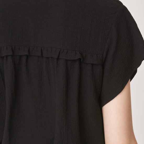 Short sleeved black top with notch neck and ruffle detail in a textured fabric