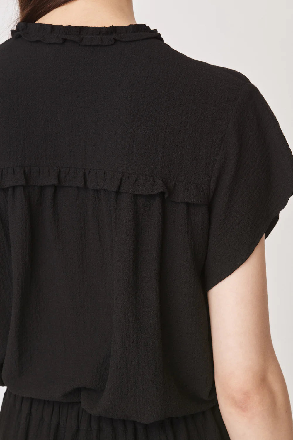 Short sleeved black top with notch neck and ruffle detail in a textured fabric