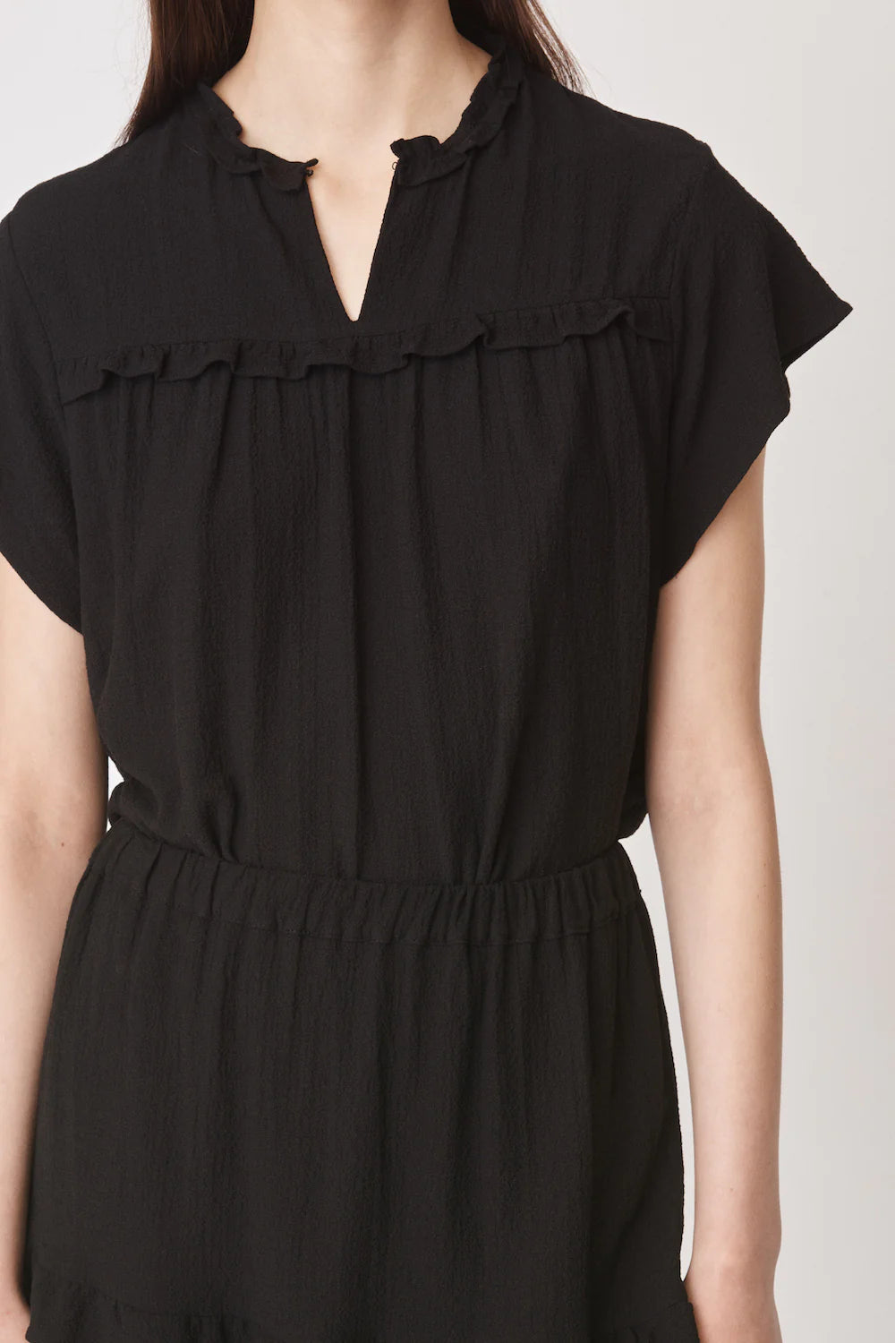 Short sleeved black top with notch neck and ruffle detail in a textured fabric