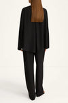 A model shown from the back wearing a black draped long-sleeve blazer and matching wide-leg trousers against a clean white studio background.