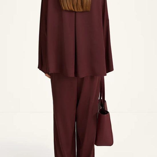 Person wearing a burgundy outfit with a matching handbag on a white background