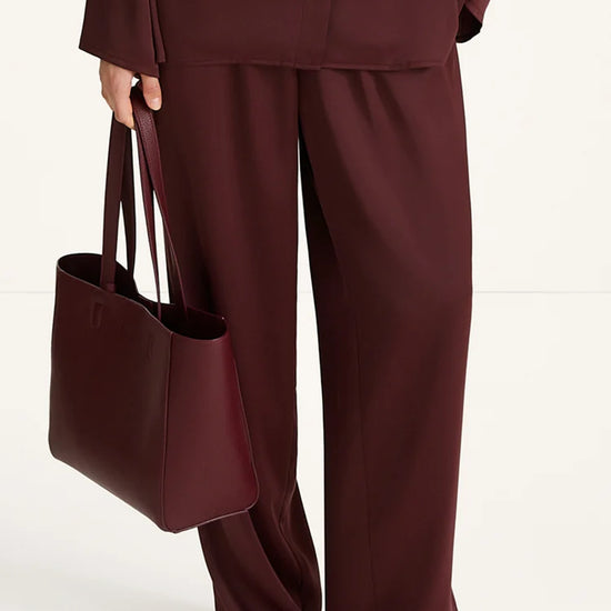 Person wearing a burgundy outfit with wide-leg pants and holding a matching tote bag on a white background