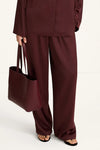 Person wearing a burgundy outfit with wide-leg pants and holding a matching tote bag on a white background