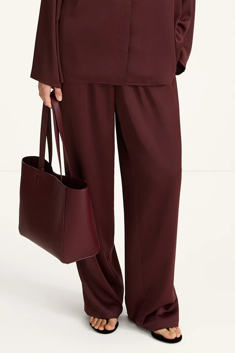 Person wearing a burgundy outfit with wide-leg pants and holding a matching tote bag on a white background