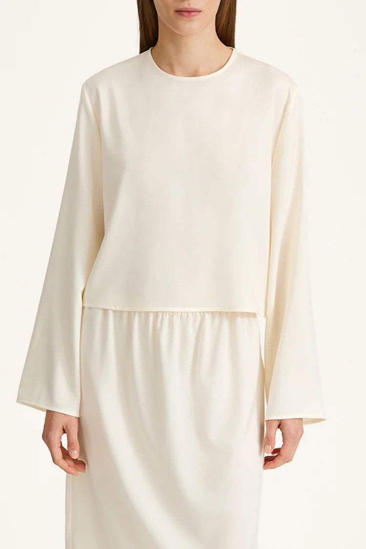 A model wearing a cream-colored long-sleeve top with a matching skirt, photographed against a clean, light off-white background.