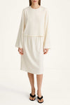 A model wearing a cream-colored two-piece set consisting of a long-sleeve cropped top and a matching knee-length skirt, paired with black flip-flop sandals against a plain white studio background.