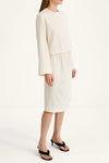 A model wearing a cream-colored two-piece set consisting of a long-sleeve cropped top and a matching midi skirt, paired with black heeled sandals against a plain white studio background.