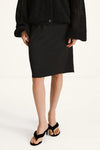 A model wearing a black knee-length skirt, a black textured cardigan, and black strappy heeled sandals, shown from the chest down against a plain white studio background.
