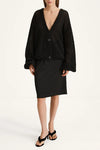 A model wearing a black open-knit cardigan with long balloon sleeves and a black pencil skirt, paired with black strappy sandals, against a plain white studio background.
