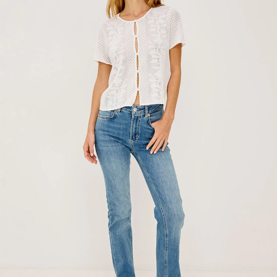 Woman wearing a white lace top by Rails and blue jeans on a plain background