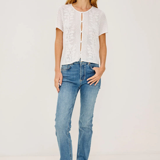 Woman wearing a white lace top and blue jeans on a plain background full outfit