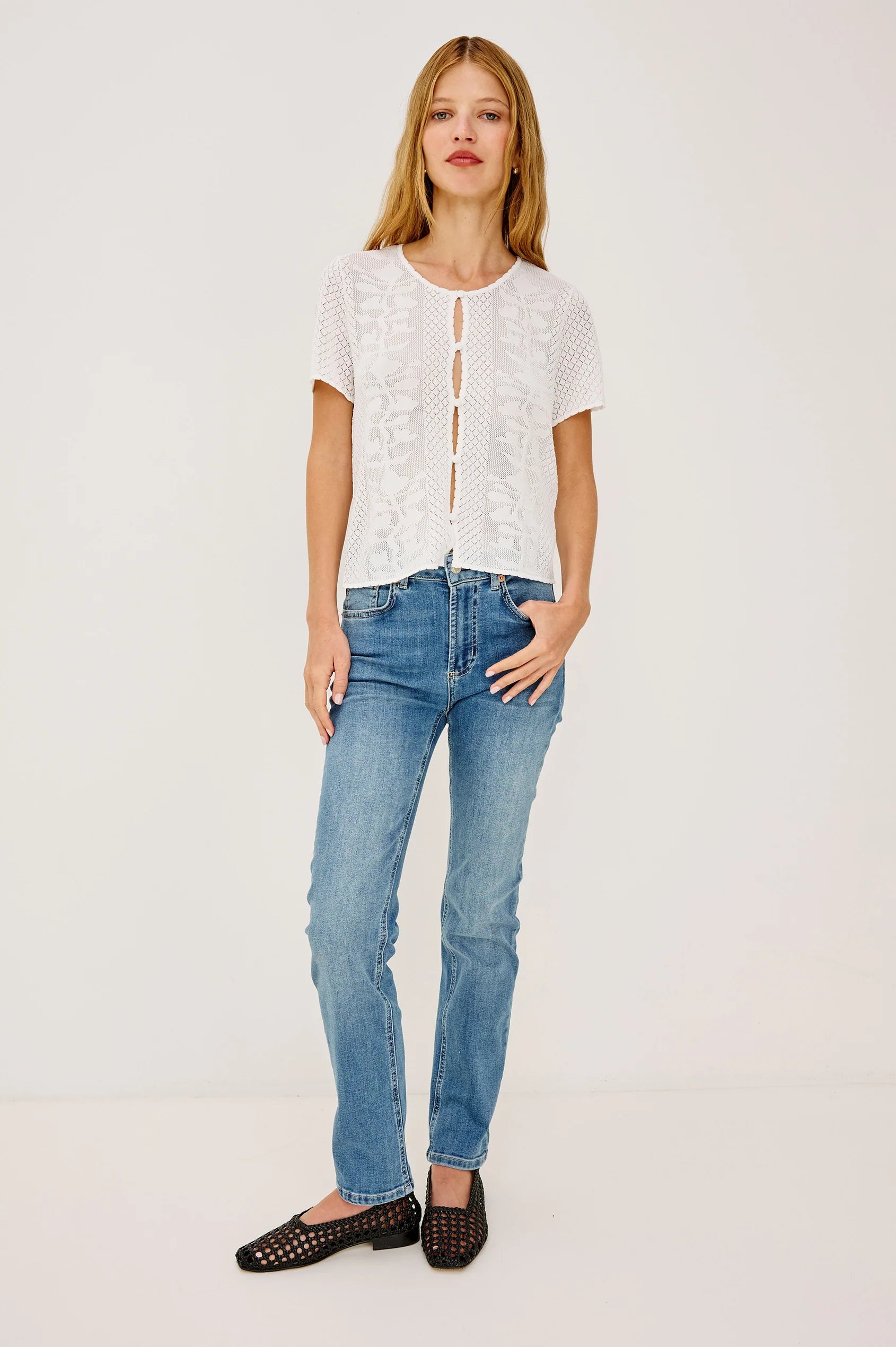 Woman wearing a white lace top and blue jeans on a plain background full outfit
