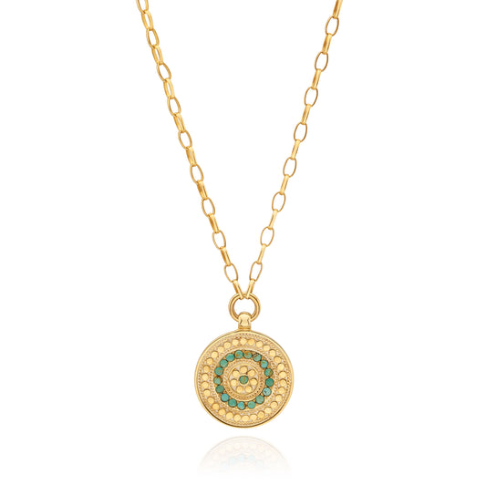 Gold necklace with a circular pendant featuring green stones on a white background